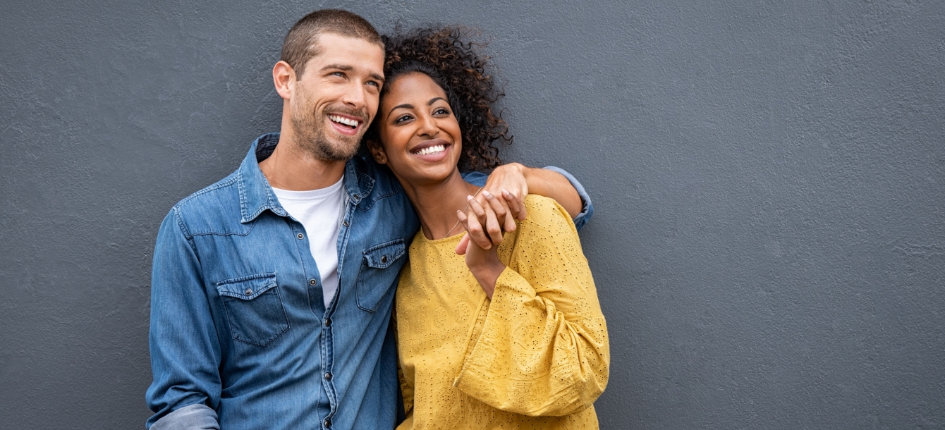 Young couple standing against wall arms around each other