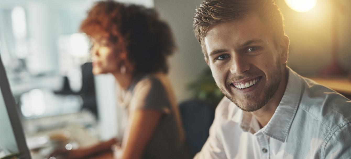 Young man smiling toward camera with colleague behind him