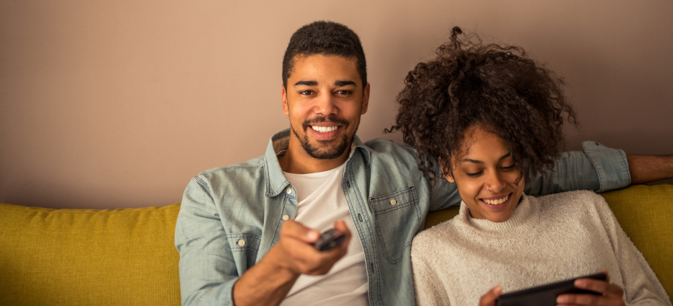 Young man and woman relaxing at home on the sofa using their tech.