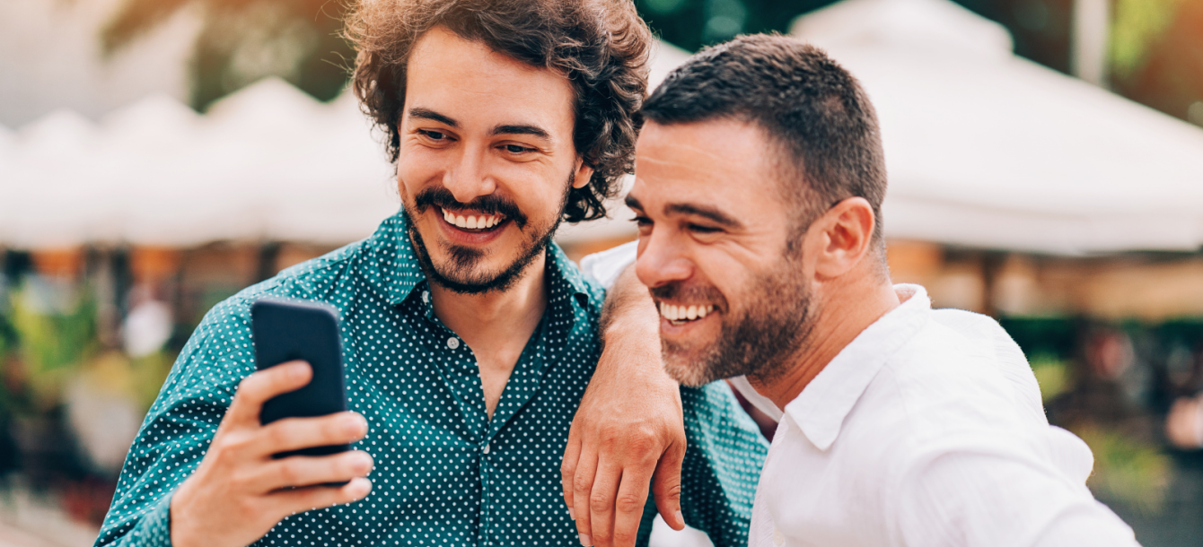 Two men outdoors smiling looking at one of their phones