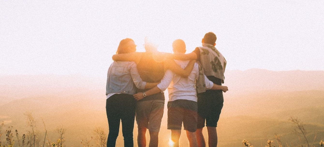 Four friends embracing while overlooking the sun setting in a valley.